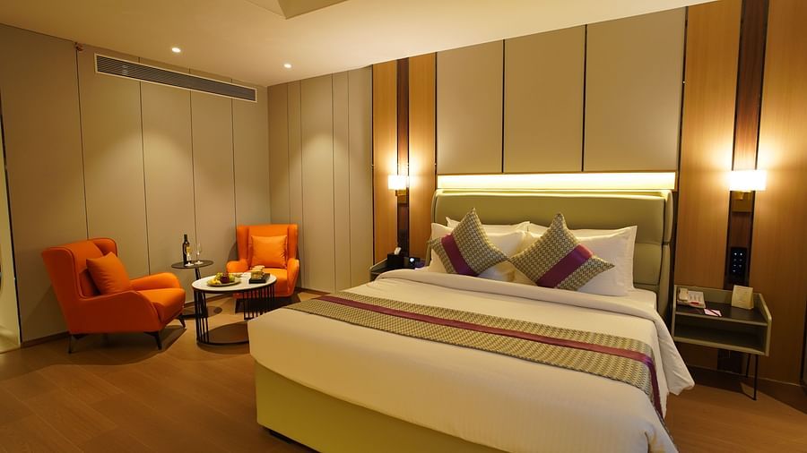 A comfortable hotel premier room showcases a king-sized bed with decorative pillows, bedside tables with lamps, and two orange armchairs near a window - The Orchid Hotel, Chandigarh