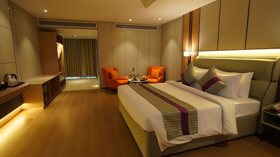 A well-appointed hotel premier room displays a king-sized bed with a striped runner, a seating area with orange chairs, and warm ambient lighting - The Orchid Hotel, Chandigarh
