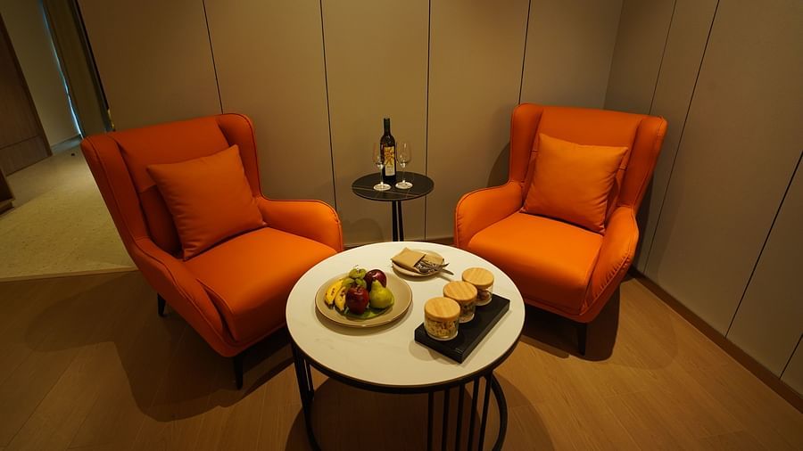 A cosy seating area in a hotel room includes two orange armchairs around a small round table with amenities, next to a window with curtains - The Orchid Hotel, Chandigarh