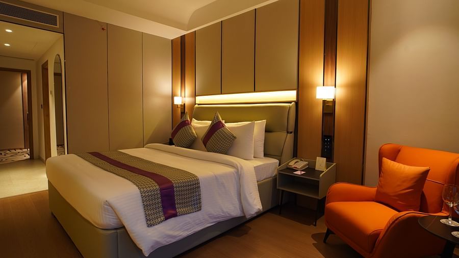 A cosy hotel club room features a single bed with patterned linens, an orange armchair with a side table, and warm lighting from bedside lamp - The Orchid Hotel, Chandigarh