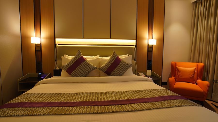 A comfortable hotel club room displays a queen-sized bed with patterned bedding, pillows, bedside lamps, and an orange armchair near the window - The Orchid Hotel, Chandigarh