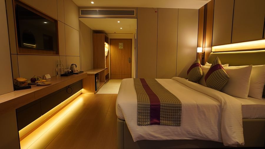 Well-lit Club Room bedroom showcasing a neatly made bed with striped accents, a long work desk with a television, and soft ambient lighting - The Orchid Hotel, Chandigarh