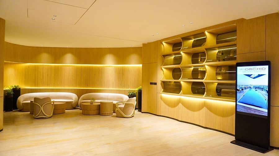 Intimate lounge corner featuring plush, curved beige seating, soft ambient lighting highlighting wooden accents, and a sleek digital screen displaying information - The Orchid Hotel, Chandigarh