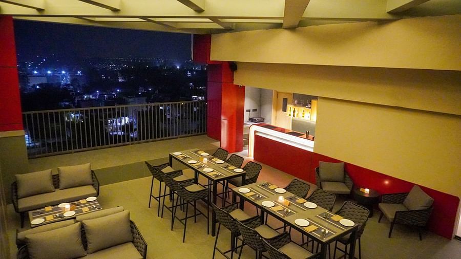 The rooftop of Skydip pool deck and bar at night, showing tables and chairs under a lit trellis, with a vibrant cityscape visible in the background - The Orchid Hotel, Chandigarh
