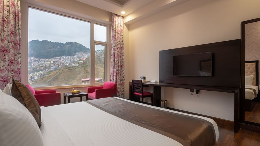 A Room in Shimla with a spacious bed and a floor to ceiling window overlooking the mountains - The Orchid Hotel Shimla