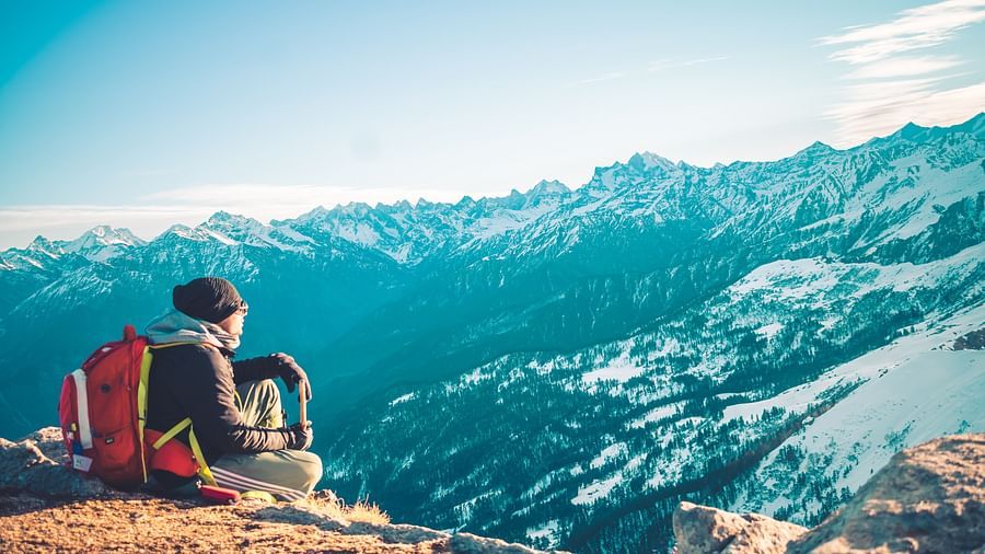 A person sitting on a mountain peak experiencing the breathtaking landscapes of Manali
