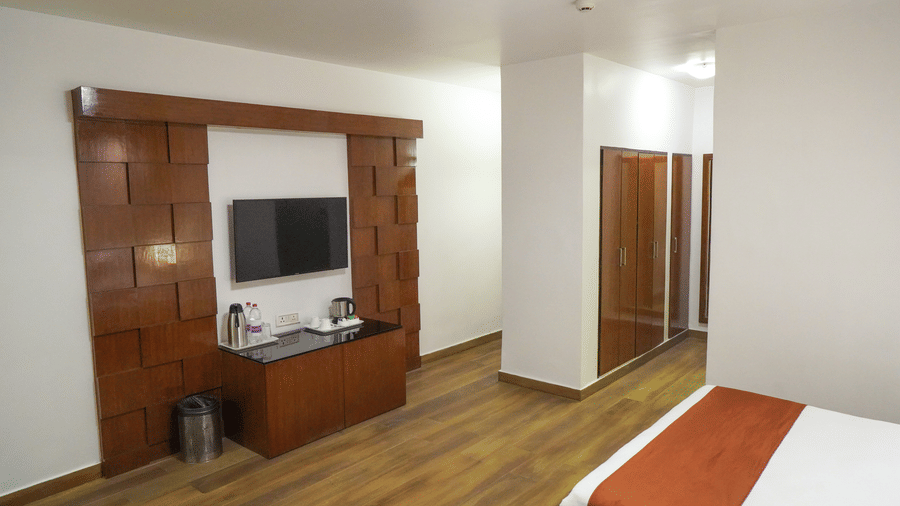 Junior Suite bedroom area featuring wooden flooring, plush double bed with orange accent facing a wall-mounted television with a table under it.