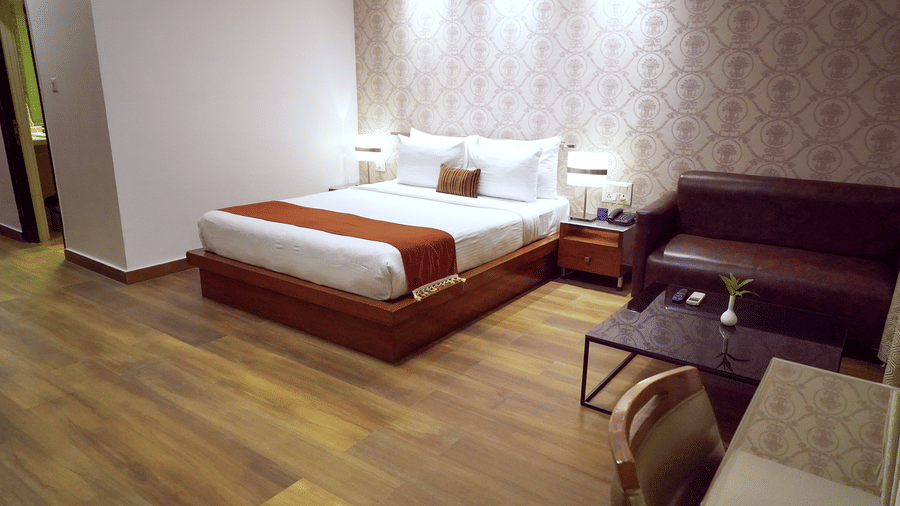 Bedroom of Junior Suite at Sarovar Portico, Bhubaneswar, showcasing the plush king size bed placed under ample overhead lighting, beside a seating area, and over wooden flooring.