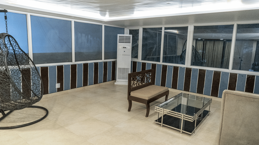 The separate seating area of the Junior Suite at Sarovar Portico, Bhubaneswar, featuring an upholstered seating chair for 2, a centre table with a glass top, and a hanging chair in a corner of the room.