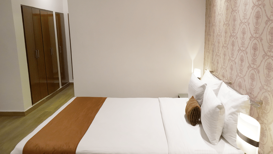 Side view of the plush double bed in the Junior Suite of Sarovar Portico, Bhubaneswar, seen with orange accents on a wooden floor.