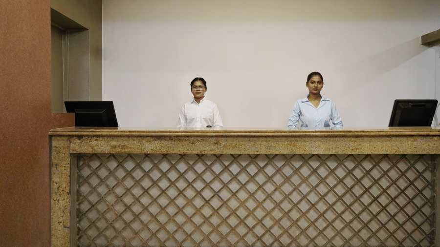The reception desk of Sarovar Portico, Bhubaneswar, seen with 2 women in formal shirts standing and facing forward.