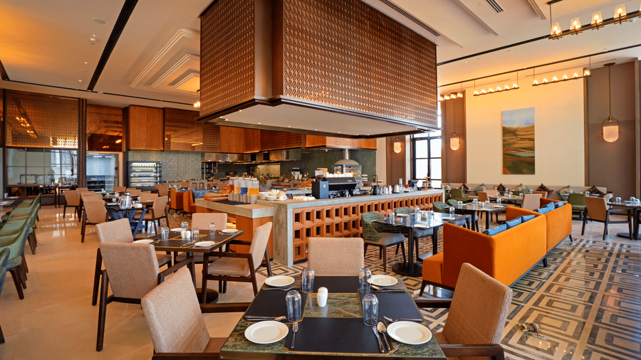 View of CHITHIRAI restaurant at The Residency Signature Madurai with a buffet counter, orange accents, wooden ceiling, and warm ambient lighting.