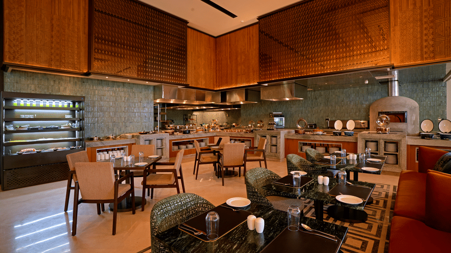 Dining tables set near a food display counter at Chithirai restaurant, The Residency Signature Madurai, lit warmly for an inviting atmosphere.