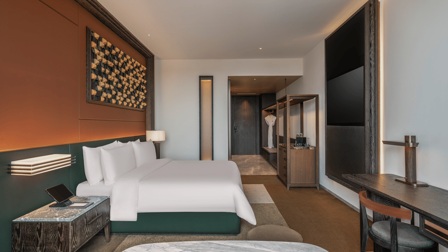 Side view of the Premium King room at The Residency Signature Madurai with a king bed, wall-mounted TV, wooden panelling, and warm ambient lighting.