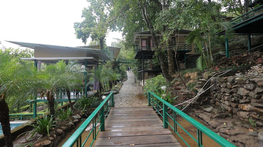 a bridge has green railings above a small stream and is leading up to cottages.