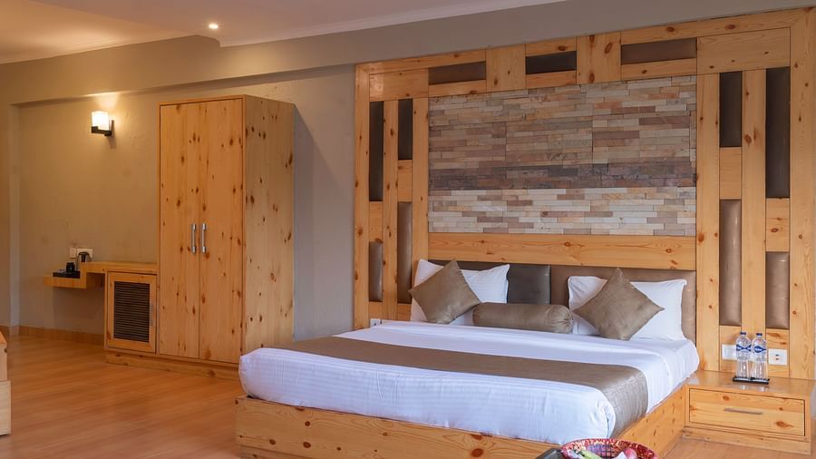 A comfortable king bed with wooden floor and wardrobe at The Tattwaa Corbett Spa & Resort.