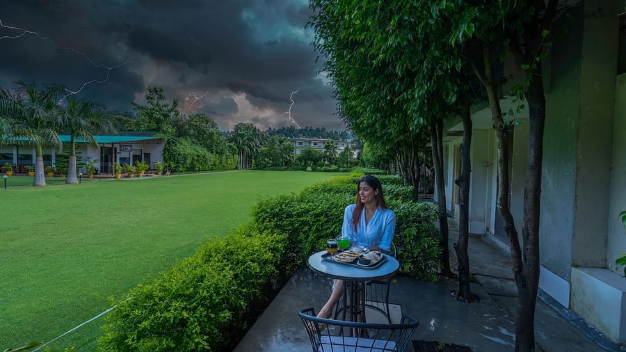 A side view of the garden area at Tattwaa, where a woman is seated, savoring tea and the beauty of nature.