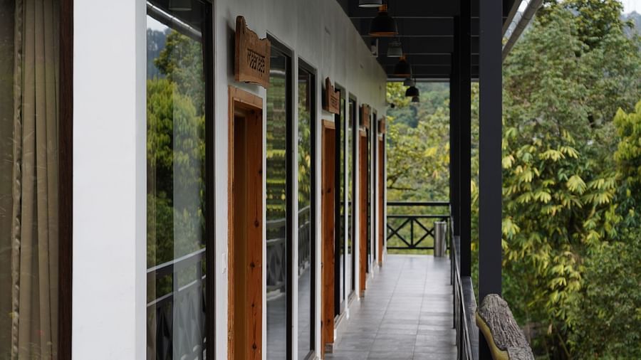 A view of a hotel building's exterior, showcasing multiple rooms with wooden doors and balconies, set against a backdrop of lush green trees, suggesting a natural and serene environment. | Premium Pool view suites | The Wild Trails Munnar