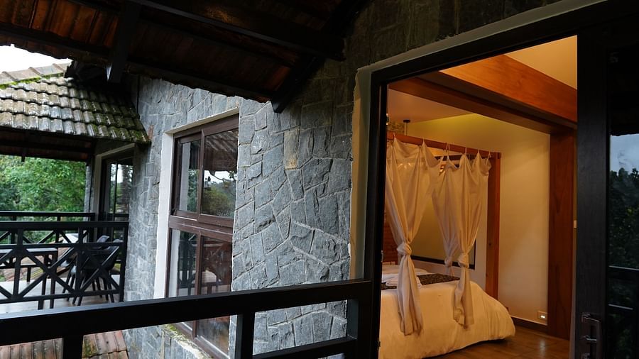 An open doorway from a balcony leading into a well-lit room with stone and wood elements. | Premium Forest View Suite with Balcony | The Wild Trails Munnar