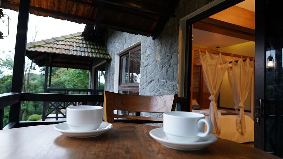 Two white cups on a dark wooden table on an outdoor balcony, with stone walls visible. | Premium Forest View Suite with Balcony | The Wild Trails Munnar