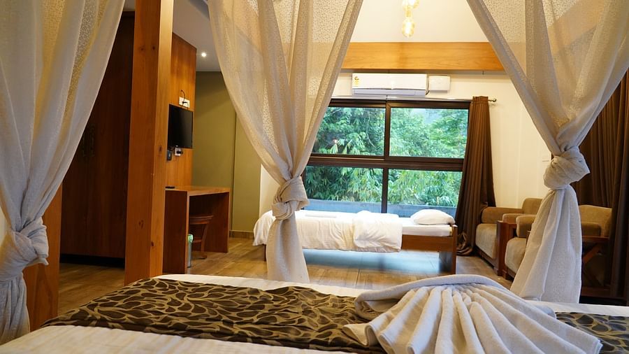 A canopy bed with white drapes in a bright room, looking out to green scenery. | Premium Forest View Suite with Balcony | The Wild Trails Munnar