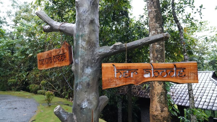 A wooden signpost with directional arrows pointing to different areas, set in a natural, wooded environment, indicating various points of interest within the hotel grounds. | The Wild Trails Munnar