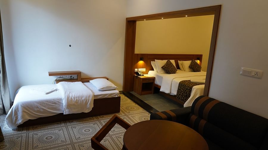A well-appointed hotel room with a comfortable bed, a sofa, and a round wooden table with chairs. The room is decorated with warm lighting and wooden accents, creating an inviting atmosphere. | Premium Pool view suites | The Wild Trails Munnar