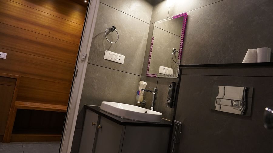 A hotel bathroom with modern grey tiling, a white sink, and a glass-enclosed shower area, indicating a clean and functional space. | Premium Pool view suites | The Wild Trails Munna