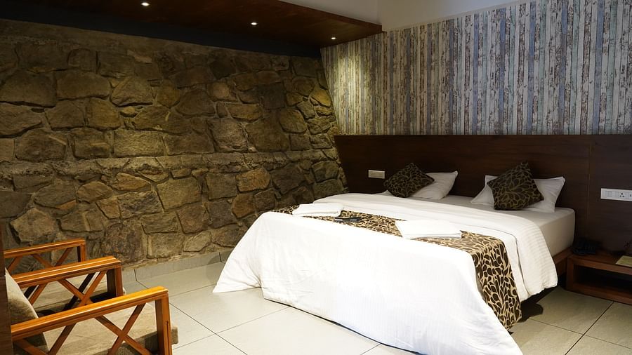 A comfortable bed with white linens and patterned throw, positioned against a stone wall. | Premium Forest view 2 Bedroom Interconnecting Suite Cottage with Balcony | The Wild Trails Munnar