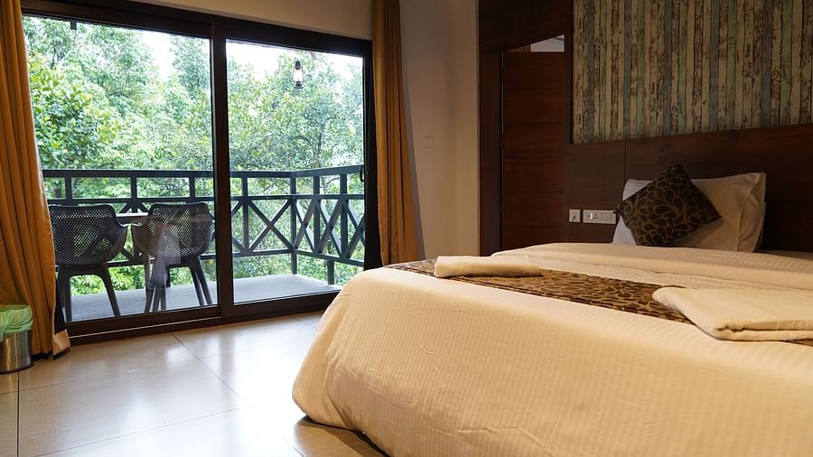 A well-appointed bedroom with a bed and large glass doors opening to a balcony with green views. | Premium Forest view 2 Bedroom Interconnecting Suite Cottage with Balcony | The Wild Trails Munnar