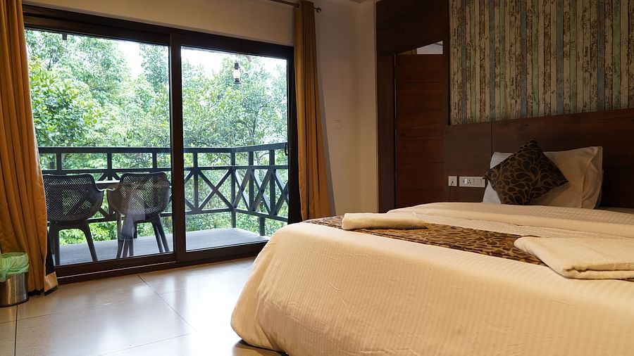 A well-appointed bedroom with a bed and large glass doors opening to a balcony with green views. | Premium Forest view 2 Bedroom Interconnecting Suite Cottage with Balcony | The Wild Trails Munnar