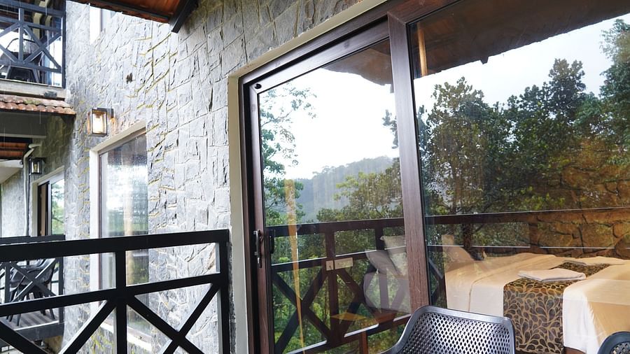 A balcony with railings offers a view of green hills, seen through a glass door. | Premium Forest view 2 Bedroom Interconnecting Suite Cottage with Balcony | The Wild Trails Munnar
