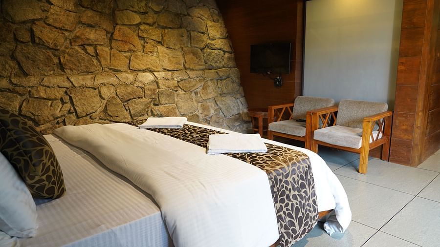 A bed with neatly folded towels, in a bedroom with a stone wall and wooden elements. | Premium Forest view 2 Bedroom Interconnecting Suite Cottage with Balcony | The Wild Trails Munnar