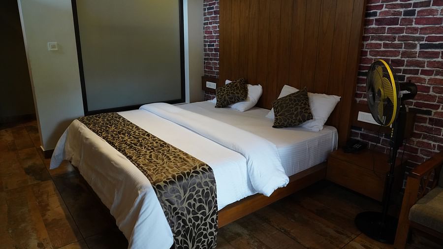 A comfortable bed with white and patterned covers, and a dark wooden headboard. | Premium Forest View Cottage With Balcony | The Wild Trails Munnar