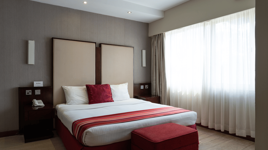 The close up of a double bed with red accents and a bed bench inside the Club Room at The Zehneria, Nairobi.