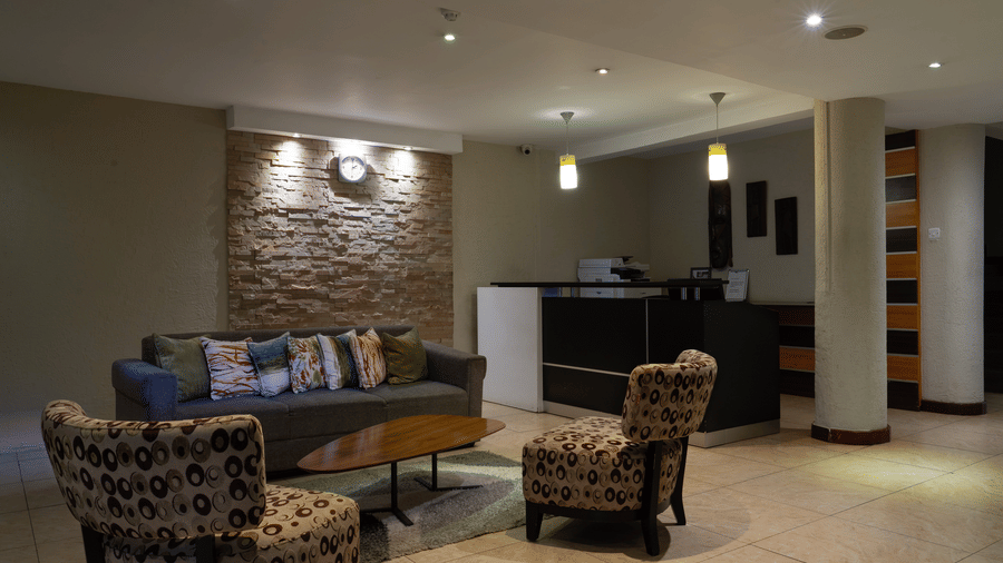 The wide angle view of the lobby area at The Zehneria, Nairobi, featuring a chair, two couches, a teapoy, and a reception desk.
