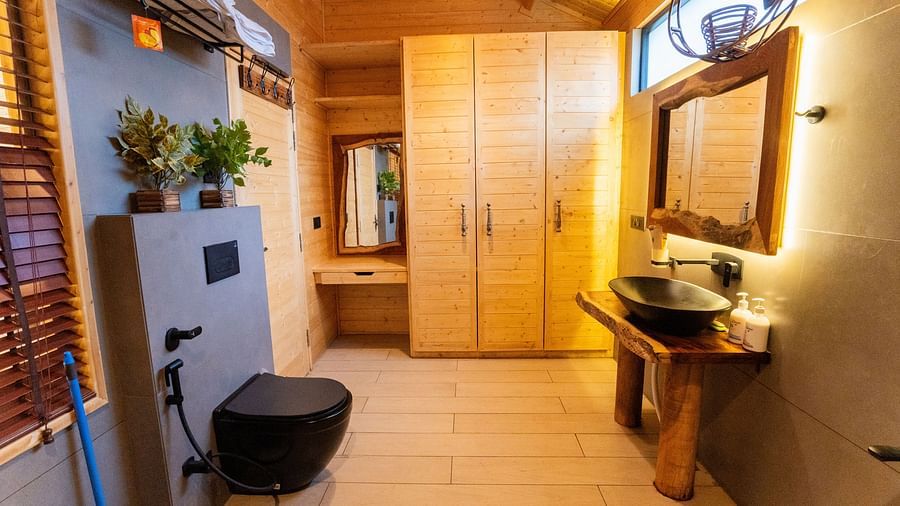 A modern bathroom at Themis Farm House features a black toilet, a unique dark sink on a wooden stand with a mirror, light wood cabinets, and a window with wooden blinds, creating a stylish space.