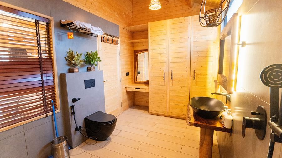 A modern bathroom features a black toilet, a unique dark sink on a wooden stand, light wood cabinets, and a window with wooden blinds at Themis Farm House.
