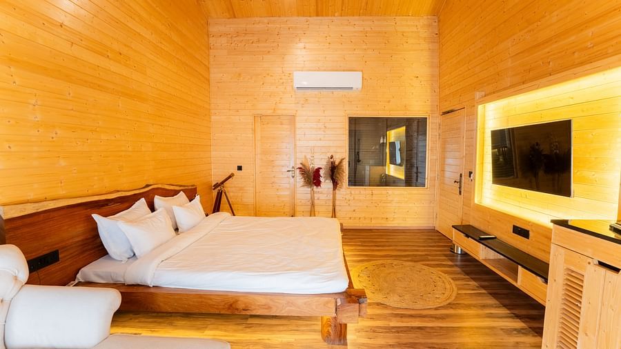 Themis Farm House features warm wooden panelling, a double bed with white linens, a wall-mounted television with ambient lighting, and a glimpse into the bathroom.