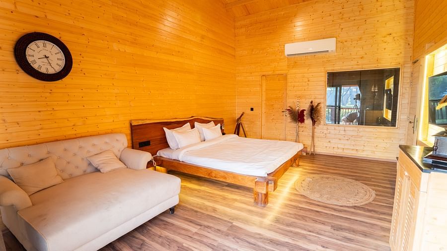 Cosy wooden bedroom with a large bed, plush sofa, wall clock, soft lighting, and modern decor at Themis Farm House.