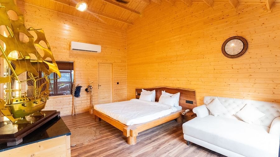 Cosy wooden bedroom at Themis Farm House featuring a large bed, white sofa, modern lighting, wooden floors, and rustic-chic decor.