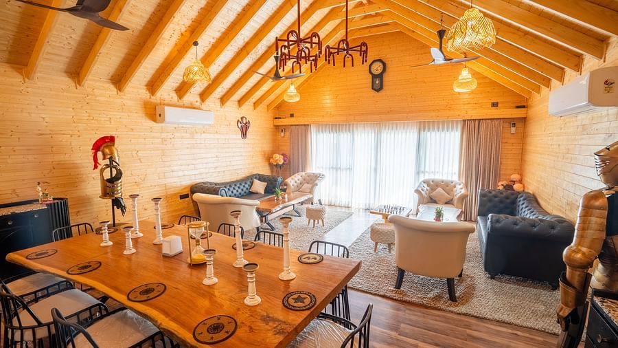 A spacious dining area with a high wooden ceiling features a long wooden dining table with chairs, alongside a comfortable lounge area with sofas and armchairs at Themis Farm House.