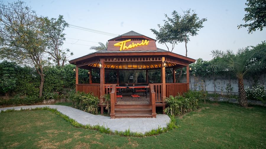 A wooden gazebo at Themis Farm House with a sign reading Themis stands on a green lawn surrounded by trees.