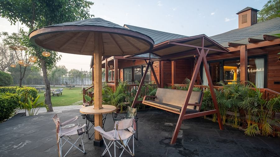 An outdoor relaxation area, at Themis Farm House features a patio set with an umbrella and chairs, alongside a wooden swing bench, surrounded by greenery.