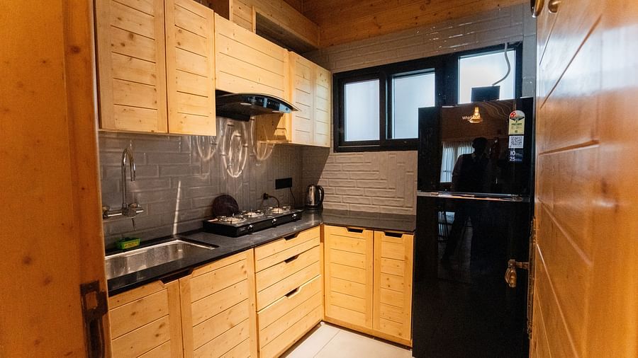 A compact kitchen area features light wooden cabinets, a dark countertop with a sink and hob, a black refrigerator, and a window at Themis Farm House