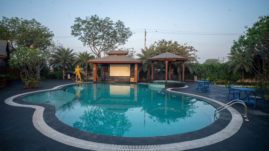 A tranquil swimming pool at Themis Farm House is surrounded by lush greenery and relaxation areas under a clear evening sky.