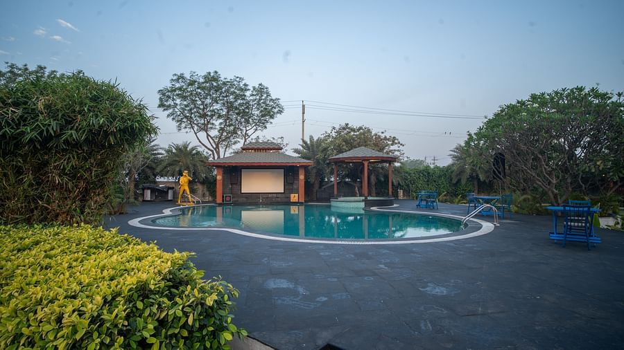 Outdoor swimming pool surrounded by lush greenery, trees, and cosy poolside gazebos at Themis Farm House under a clear blue sky.