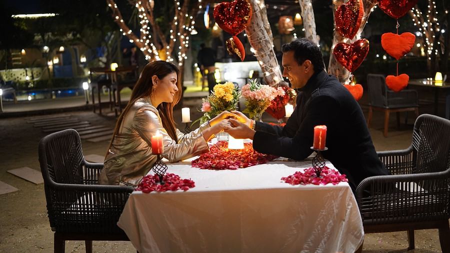A couple enjoying a candlelight dinner at Themis Mudhouse, looking at each other, with a table decorated with flowers, candles, and heart-shaped decorations in the background.