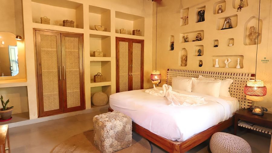 a warmly-lit Royal Villas displaying a bed with a lamp hanging by its side at Themis Mudhouse - A Nature's Retreat Resort & Wellness