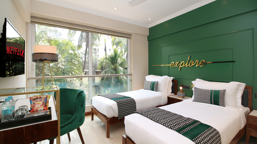 Twin beds facing the TV on the wall with a table and chair below, and large windows by the bed at Theory9 - Premium Srervice Apartments, Bandra